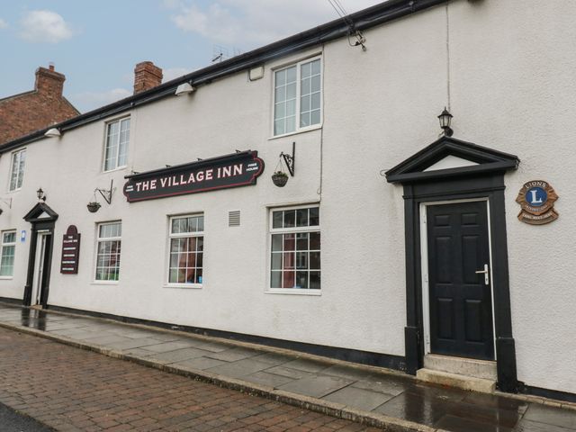 The exterior of The Village Inn with white walls black doors and windows along a paved sidewalk in Murton