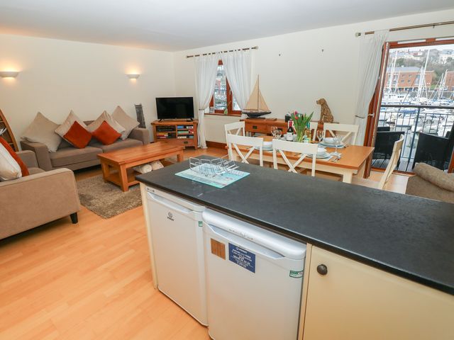 An open living and dining area with sofas and a dining table overlooking a marina at 14 Neptune House in Milford Haven