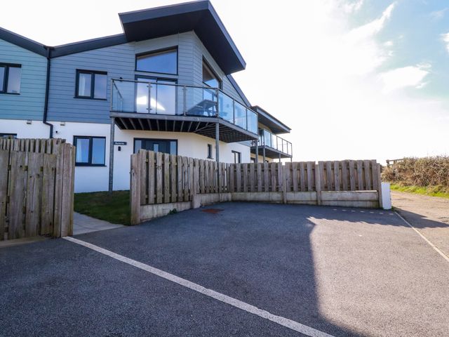 A modern house with a balcony and glass railing behind a wooden fence and driveway at Jacana in Perranporth