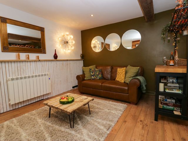 A living room with a brown leather sofa cushions a wooden coffee table with fruit and mirrors on the wall at Flat 6 Aikbank in Whitehaven