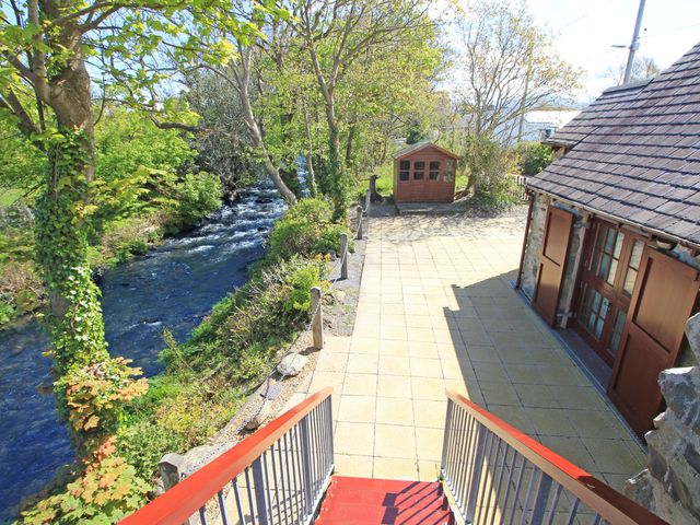 A river flowing beside a paved patio area with stairs and a wooden shed at Melin Y Cim in Caernarfon