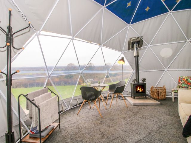 An interior view of a dome structure with a small table and two chairs a wood stove a floor lamp a coat rack and a towel rack at Meadow View - Bryn-Mawr Retreat in Brynmawr near Llanymynech