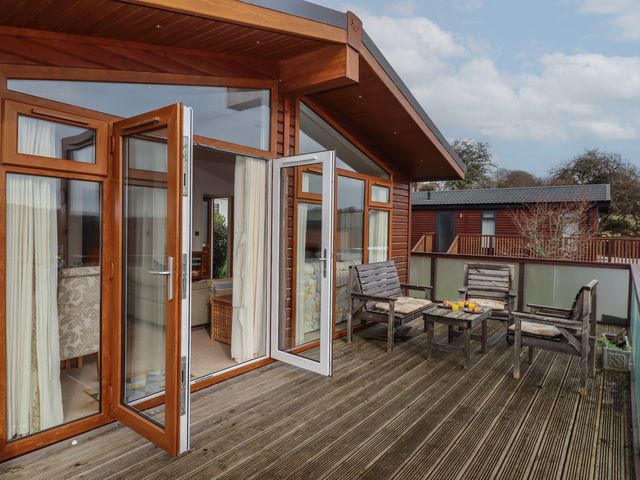 An outdoor wooden deck with four wooden chairs and a small table with drinks outside a building with large glass doors at Skyview in Newton Ferrers