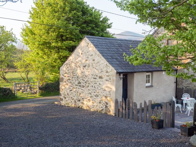 A small stone and plaster building with a slate roof next to a fenced patio with white metal chairs and tables at Cwt Mochyn in Llanberis