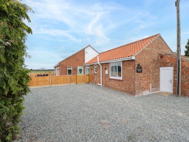 An outdoor area with a cottage and gravel driveway at Denholme in Hogsthorpe