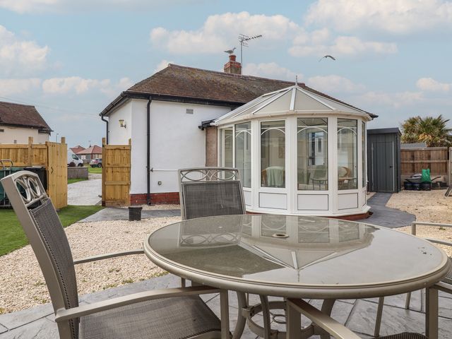 A garden with a table and chairs near a conservatory at Driftwood in Rhyl