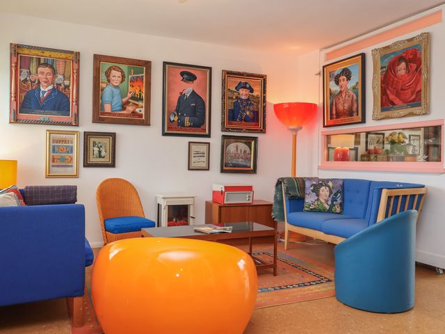A living room with blue furniture orange chair paintings on walls and a floor lamp at The Orchard Close Art House Great Livermere near Bury St Edmunds