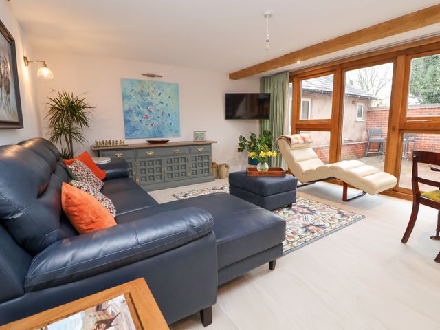 A living room with a black leather sofa and chaise lounge next to a beige recliner and large windows at Sylva Cottage Burlton near Cockshutt