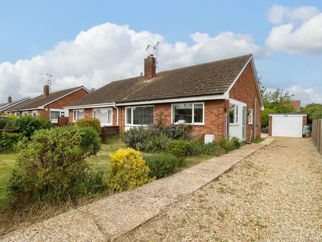 A single-story brick house with a tiled roof a front garden with shrubs and a gravel driveway leading to a garage at Little Lodge in Dersingham