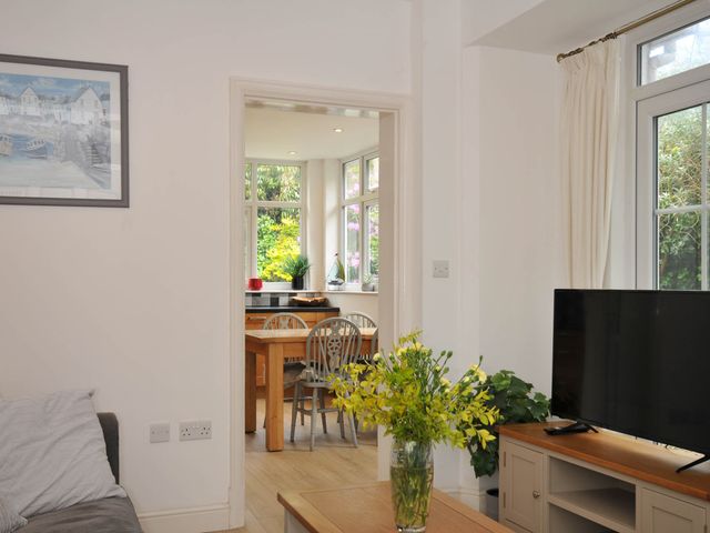 A living room with a television on a wooden cabinet and a vase of flowers on a table looking into a dining area with a wooden table and chairs at Falmouth Bay 1 in Falmouth