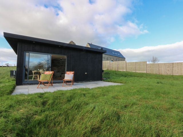 An outdoor area with chairs and a black building at Tithe Barn Lodge Capel Mawr near Malltraeth