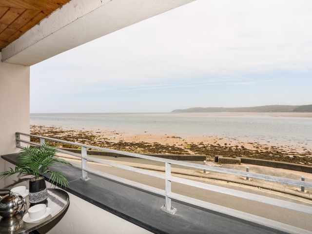 A balcony with a table holding a plant and tea set overlooking a beach and sea at 2 The Quay in Pentraeth