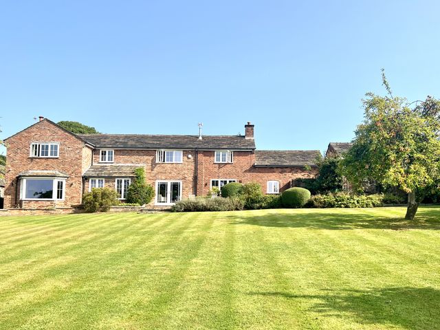 A house with a lawn and trees at Higher Park Farm in Alderley Edge