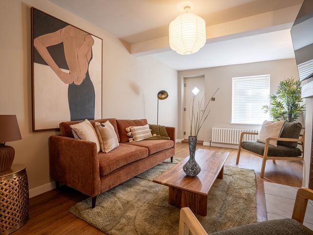 A living room with a brown sofa, wooden coffee table with a vase, an armchair, a floor lamp, and a large painting at Driftwood in Kessingland