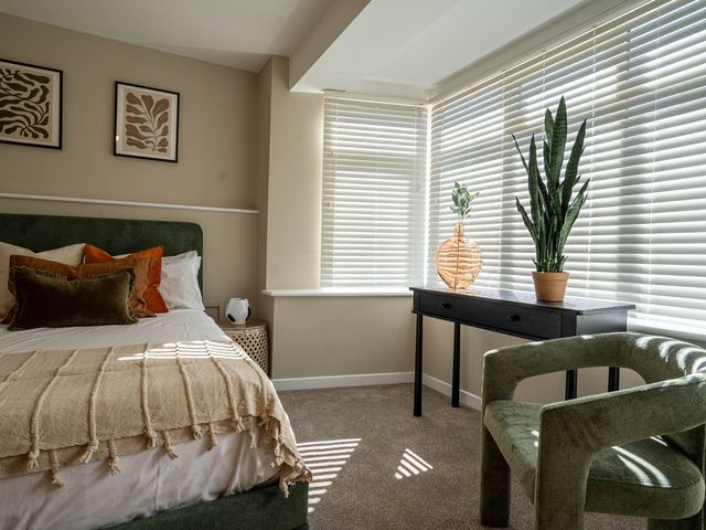 A bedroom with a bed pillows and blanket a black table with plants and a green chair by a window with blinds at The Reef in Kessingland