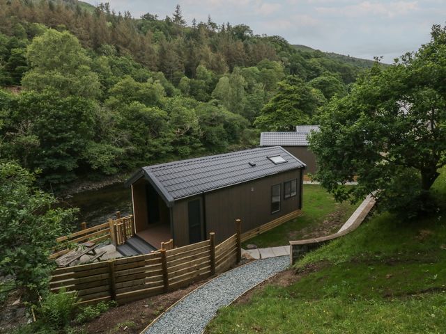 Two cabins near a river with trees in the background at Dubs Luxury Family Pod in Keswick