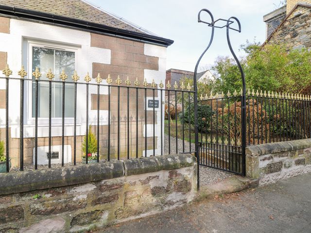 A black metal fence with gold details and an arched gate in front of a stone house at Beadles Cottage in Blairgowrie