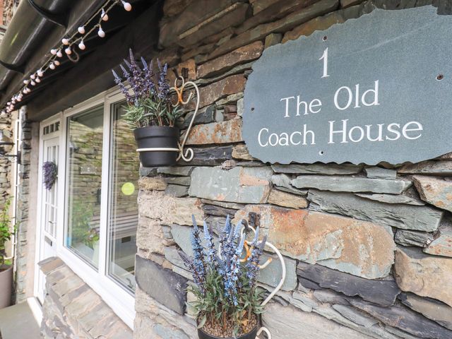 Exterior stone wall with a door and window and flower pots hanging near a sign that says 1 The Old Coach House Ambleside