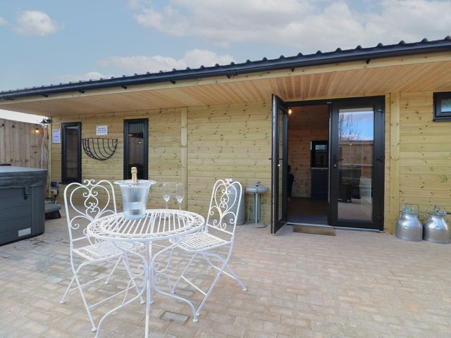 An outdoor patio with a white metal table and chairs a champagne bucket with bottle and two glasses outside a wooden building with open double doors at The Parlour in Church Broughton near Hatton Derbyshire