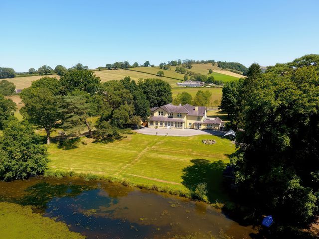 An outdoor view of a house with a lawn and lake at The Retreat at Glanrannell Park House Llansawel
