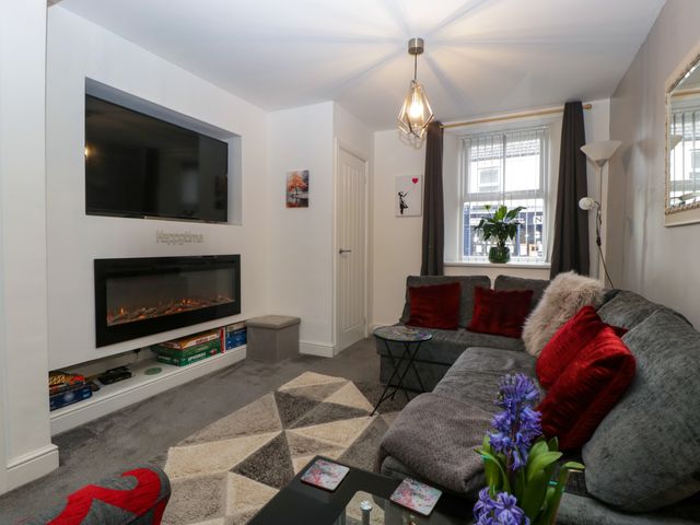 A living room with a large grey sectional sofa with red cushions a wall-mounted television above a fireplace and a window with closed curtains at Colliers Cottage in Cinderford