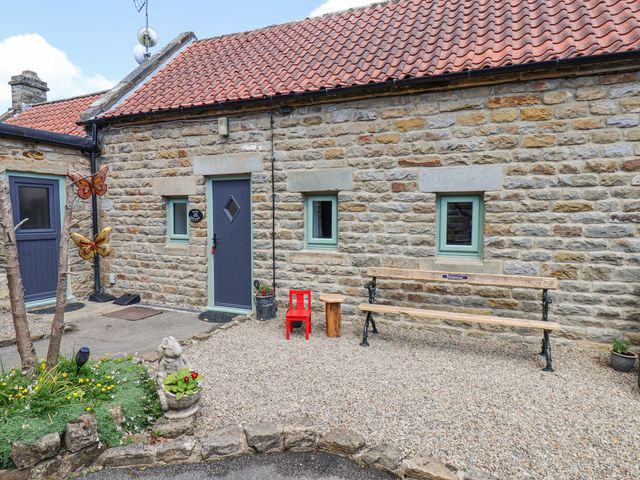 An exterior stone wall of a building with a blue door and windows a wooden bench a small wooden stool a red child size chair and garden decorations at Wayside Farm Dairy Cottage Cloughton near Burniston