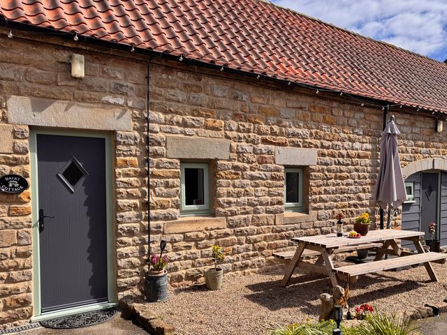 A patio area with a table and umbrella at Wayside Farm Dairy Cottage Cloughton near Burniston