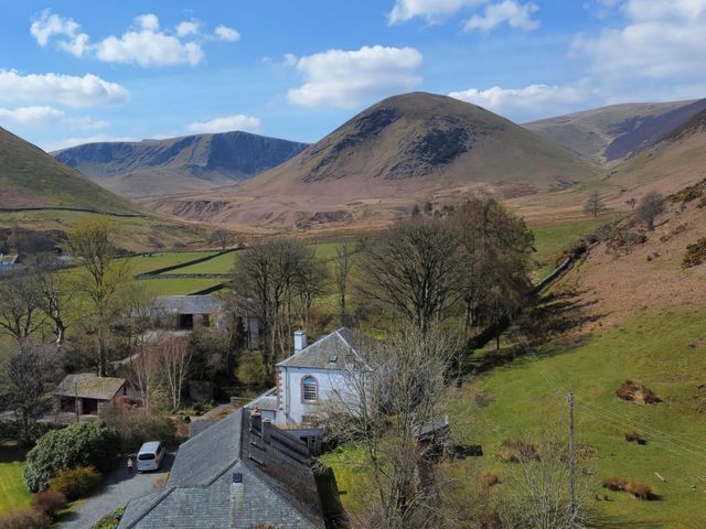 A rural landscape with houses cars trees and hills under a blue sky at The School in Mungrisdale near Caldbeck