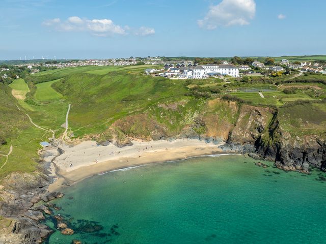 A beach with people on sand and turquoise water near cliffs and a town on green hills at Villa 5 in Mullion
