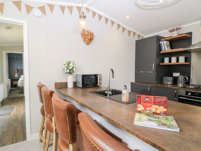 A kitchen with a counter and brown leather bar stools with a sink microwave and kitchen cabinets at The Gallops in Chipping Norton