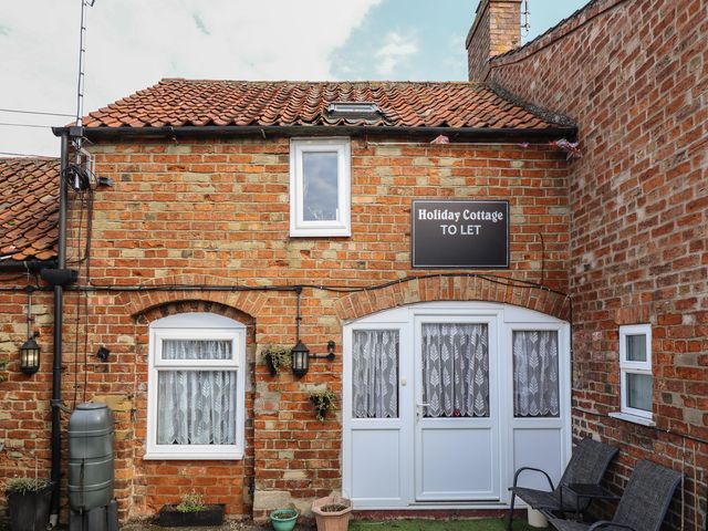 A brick holiday cottage with white doors and windows and outdoor seating at The Old Stables in Burgh Le Marsh