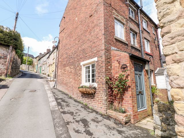 A brick house on a narrow street with stone and brick buildings along the hill at The Beehive in Wirksworth