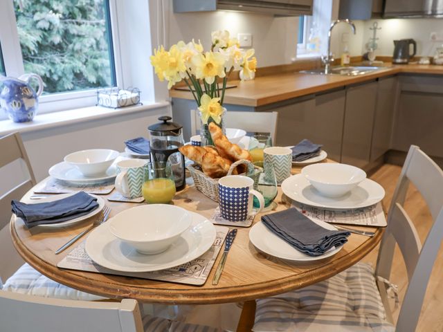 A kitchen table set for breakfast with bowls, mugs, croissants, orange juice, and flowers at Bradleys Barn in Boxted near Great Horkesley