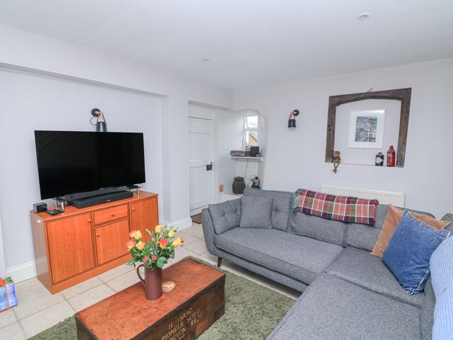 A living room with a gray sectional sofa and cushions a wooden cabinet with a TV on top and a wooden coffee table with flowers at Joymead in Malborough