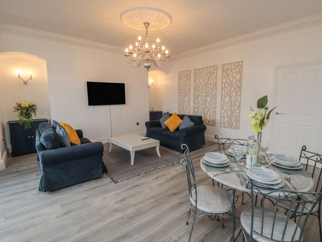 A living room with sofas a coffee table a wall-mounted TV a dining table with set plates and flowers at The Sea Escape in Saltburn-By-The-Sea