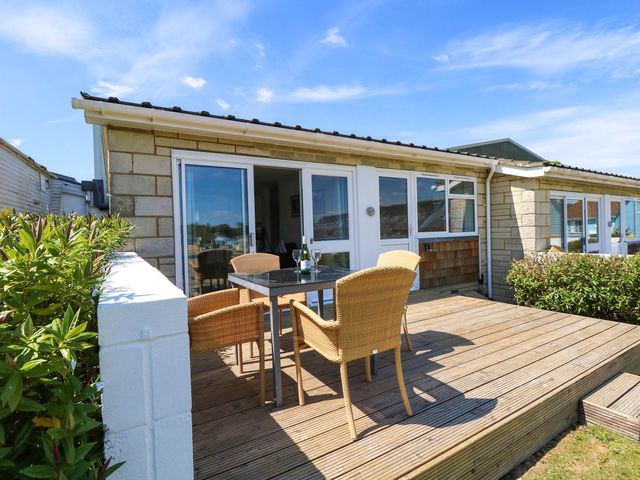 An outdoor wooden deck with a table and four wicker chairs outside a stone house at Cape 14 in Yarmouth