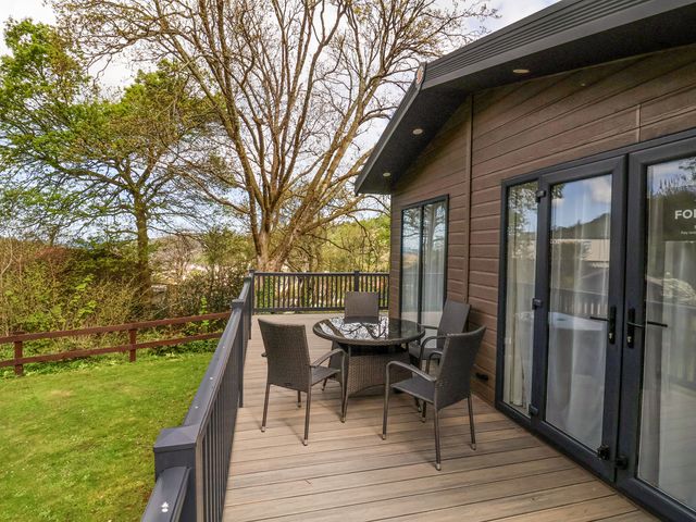 An outdoor deck with a round glass table and four chairs next to a building with large glass doors at 16 Manleigh Park in Combe Martin