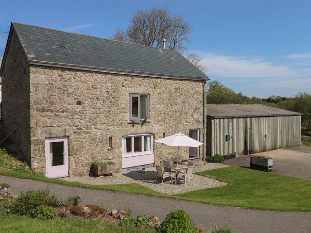 A stone barn with outdoor table and chairs under an umbrella next to a wooden shed at Puddaven Barn in North Bovey near Chagford