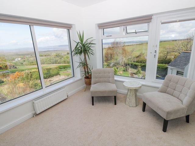 A sitting area with two beige chairs a small round table and large windows overlooking a garden and countryside at Burry House in Llanmorlais