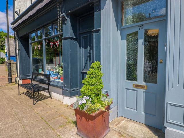 A building entrance with a blue door numbered 72 a large flower pot with plants and a black bench outside a building at The Loft in Ystradgynlais