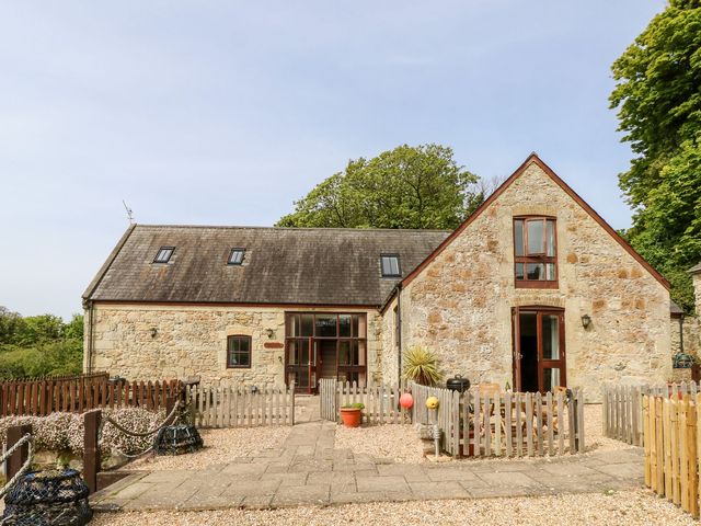 A stone building with a pitched roof and wooden fences around a gravel area near trees at The Lobster Pot near Ventnor