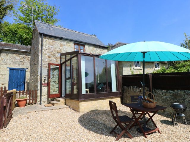 A small stone cottage with a glass porch and a patio area with table chairs umbrella and a barbecue at Fisherman's Cottage near Ventnor