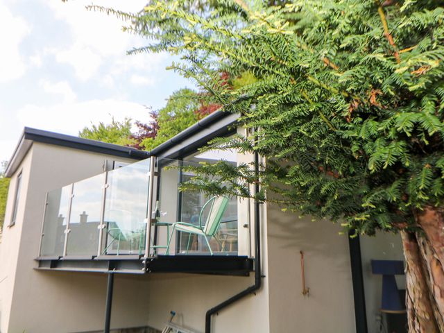 An outdoor glass balcony with two green chairs and a small table next to a cream building with a tree nearby at Yew Tree Cottage in Matlock