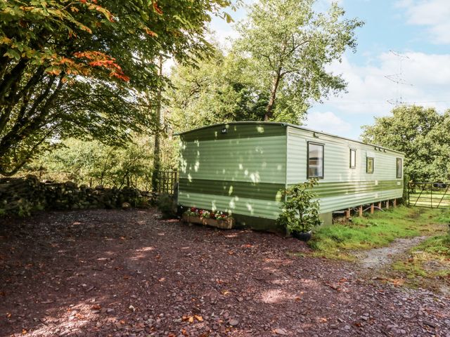 A green caravan surrounded by trees and gravel at Meadow Island Caravan 