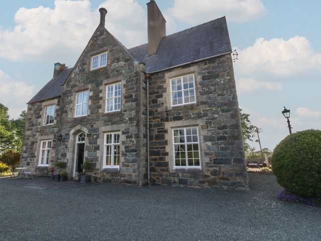 A stone house with multiple white-framed windows and a gravel driveway at Glasfryn in Llandwrog