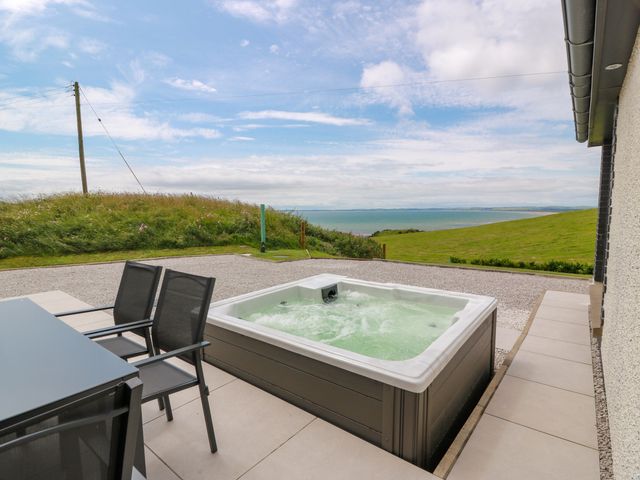 A hot tub and outdoor dining area overlooking the sea at Balcarry Barn in Glenluce