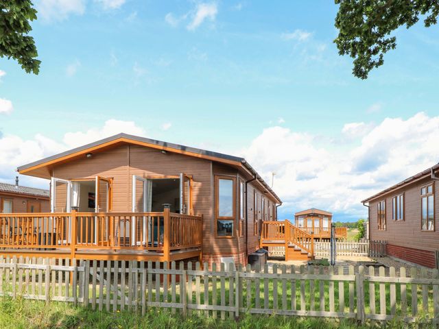 A wooden lodge with a deck and fenced outdoor area at Oak Tree Holiday Lodge in Stonham Aspal