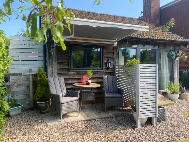A small outdoor seating area with two chairs and a table under an awning beside a wooden house at The Pheasant's Nest in Welland near Upton Upon Severn