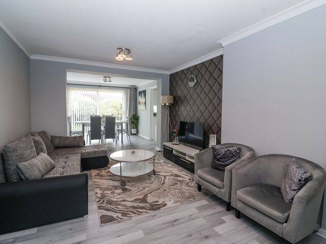 A living room with a grey sofa armchairs round coffee table and TV unit at Zadena in Timsbury
