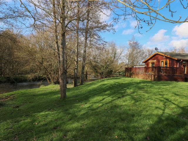 A lodge with a deck near a river surrounded by trees at Riverside Lodge 3
